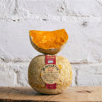 Mimolette cheese with a pumpkin half on top against a textured white wall.