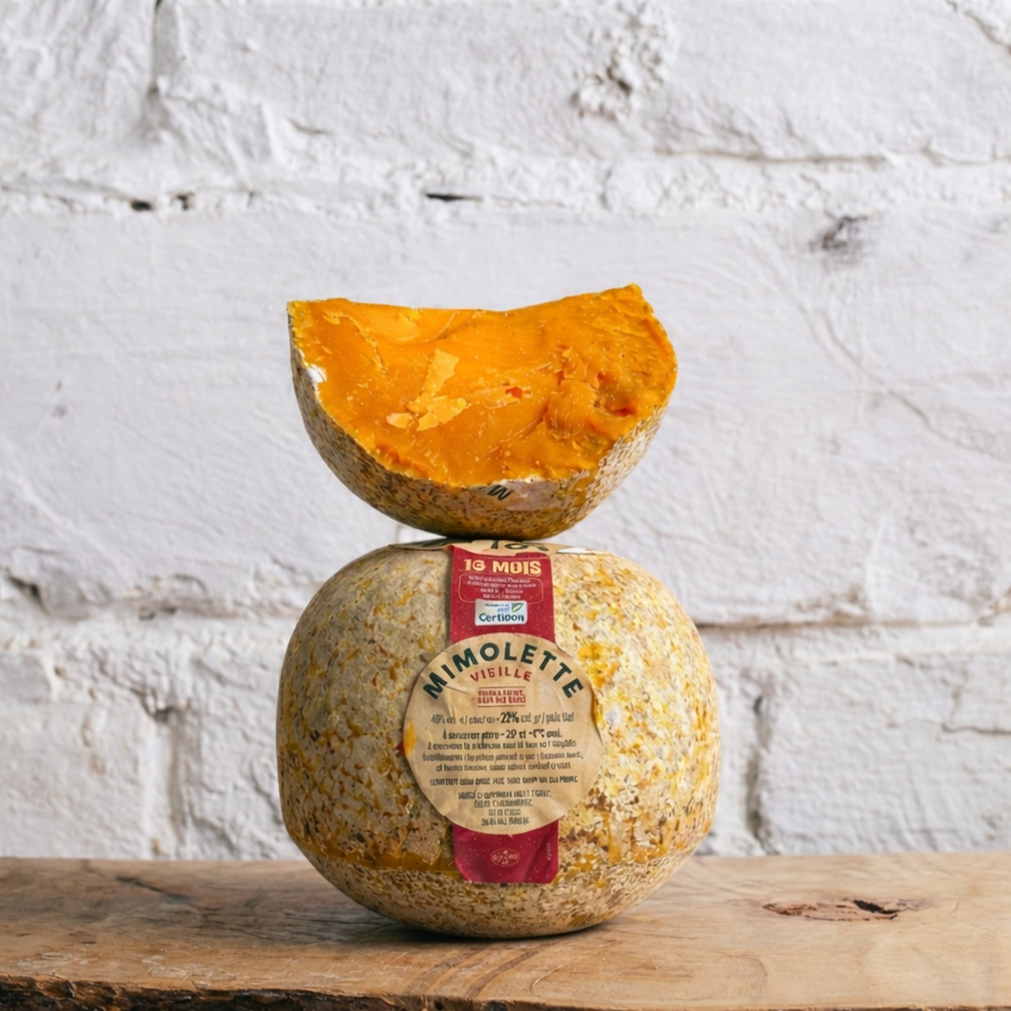 Mimolette cheese with a pumpkin half on top against a textured white wall.