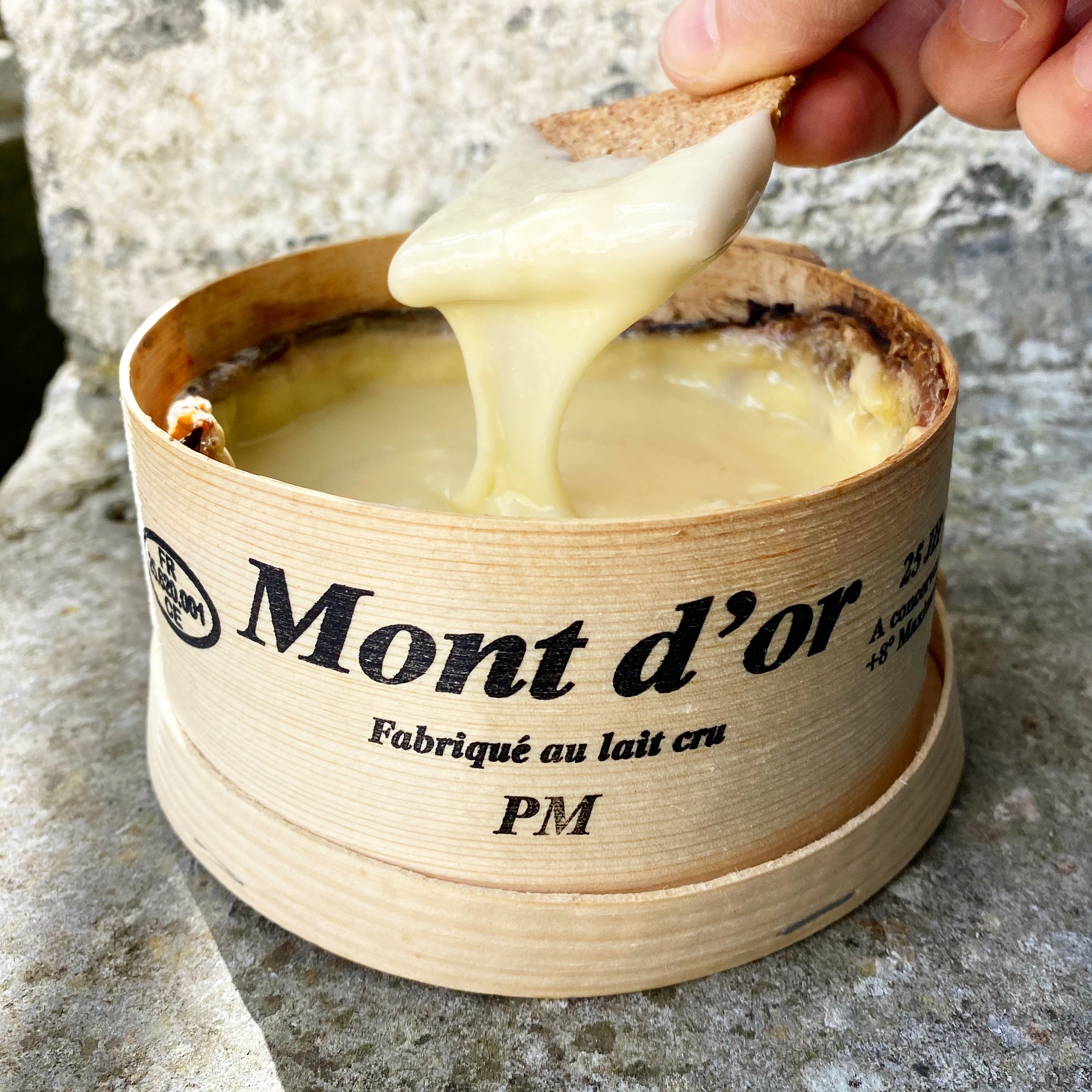 Mont d'or cheese being scooped with a wooden knife on a stone surface