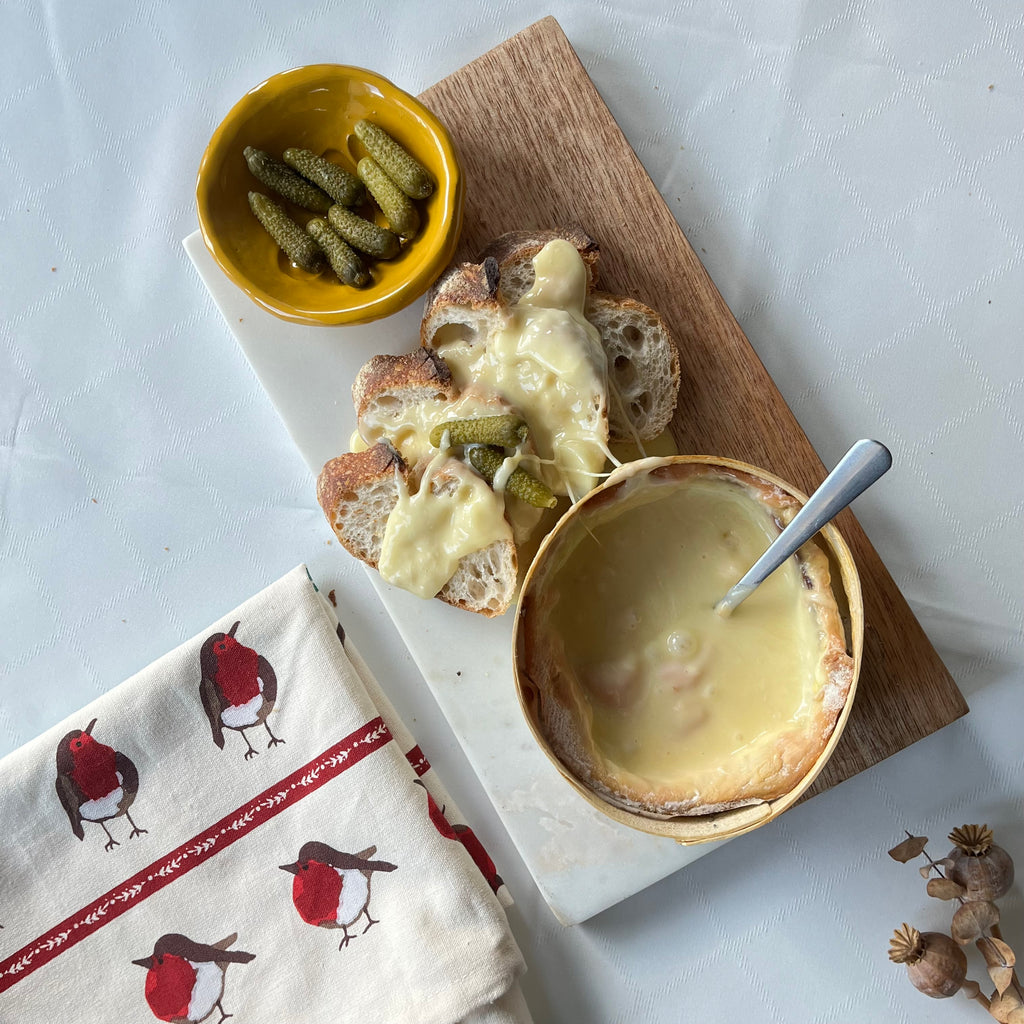 Plated dish with bread, cheese, and pickles on a marble slab with a towel and small bowl of pickles.