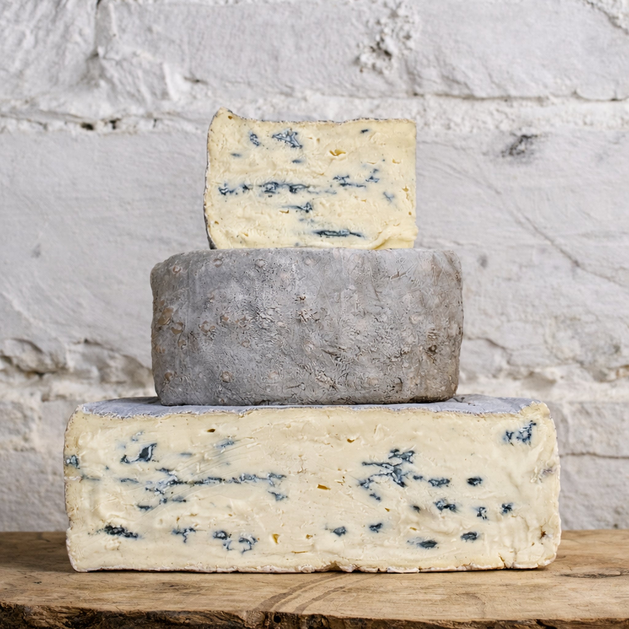 Three types of blue cheese stacked on a wooden surface with a marble background
