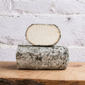 Block of cheese with a slice on top on a wooden surface with a light gray background
