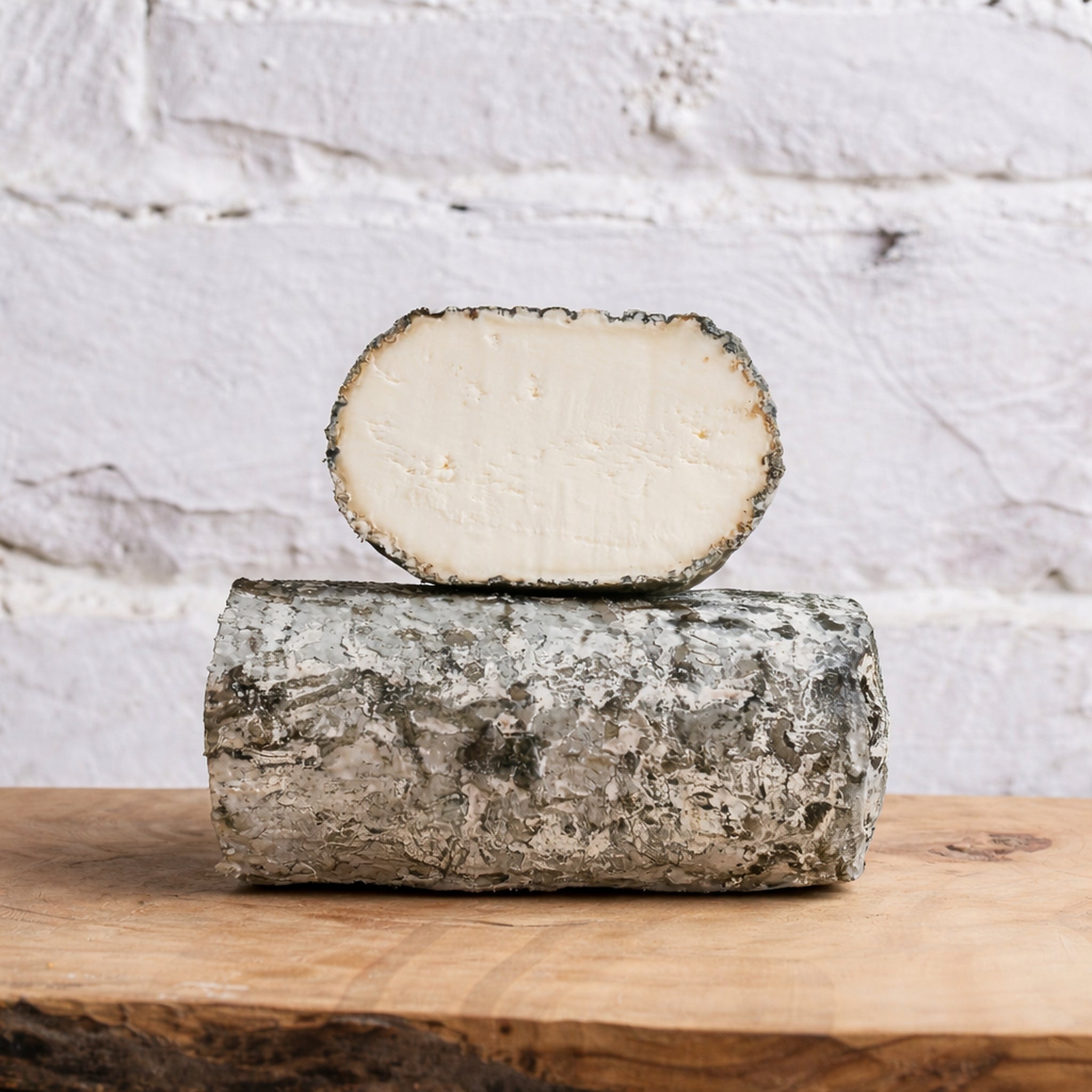 Block of cheese with a slice on top on a wooden surface with a light gray background