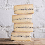 Stack of blue-streaked cheese on a wooden surface with a white textured background