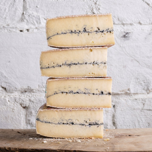 Stack of blue-streaked cheese on a wooden surface with a white textured background
