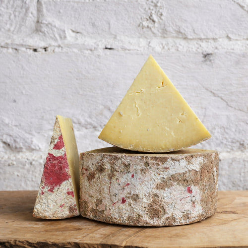 Three types of cheese on a wooden board with a textured white background