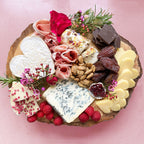 Heart themed grazing board with cheeses, charcuterie, nuts and pink flowers