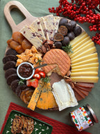 Assorted cheese, fruits, and crackers on a wooden board with a jar of jam and red berries in the background.