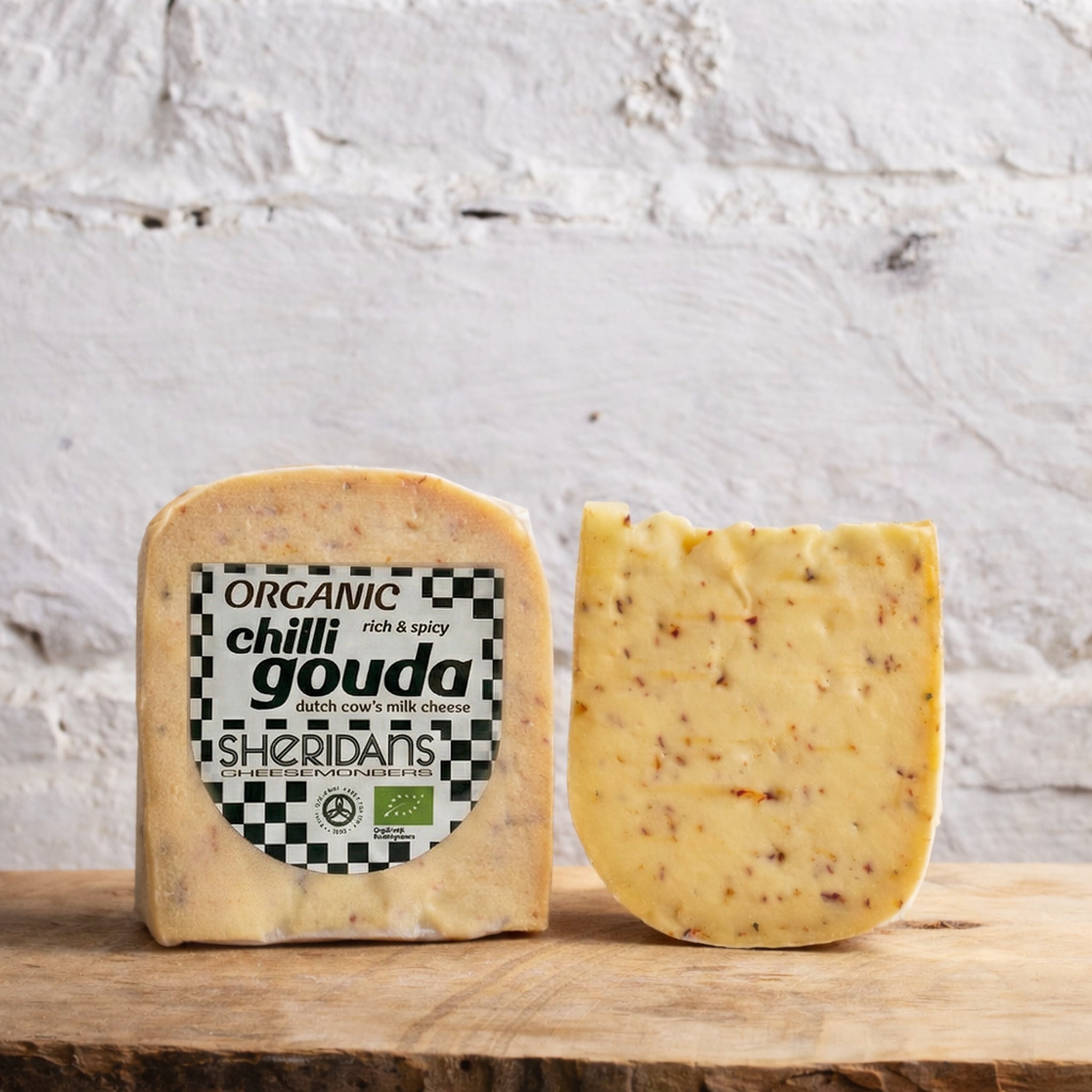 Two blocks of organic chilli gouda cheese with a Sheridan's label on a wooden surface.