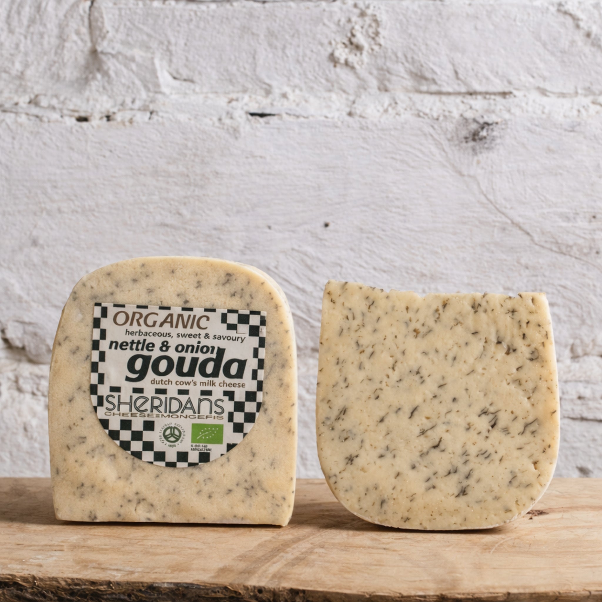 Two blocks of gouda cheese with a Sheridan's label on a wooden surface against a textured white wall.
