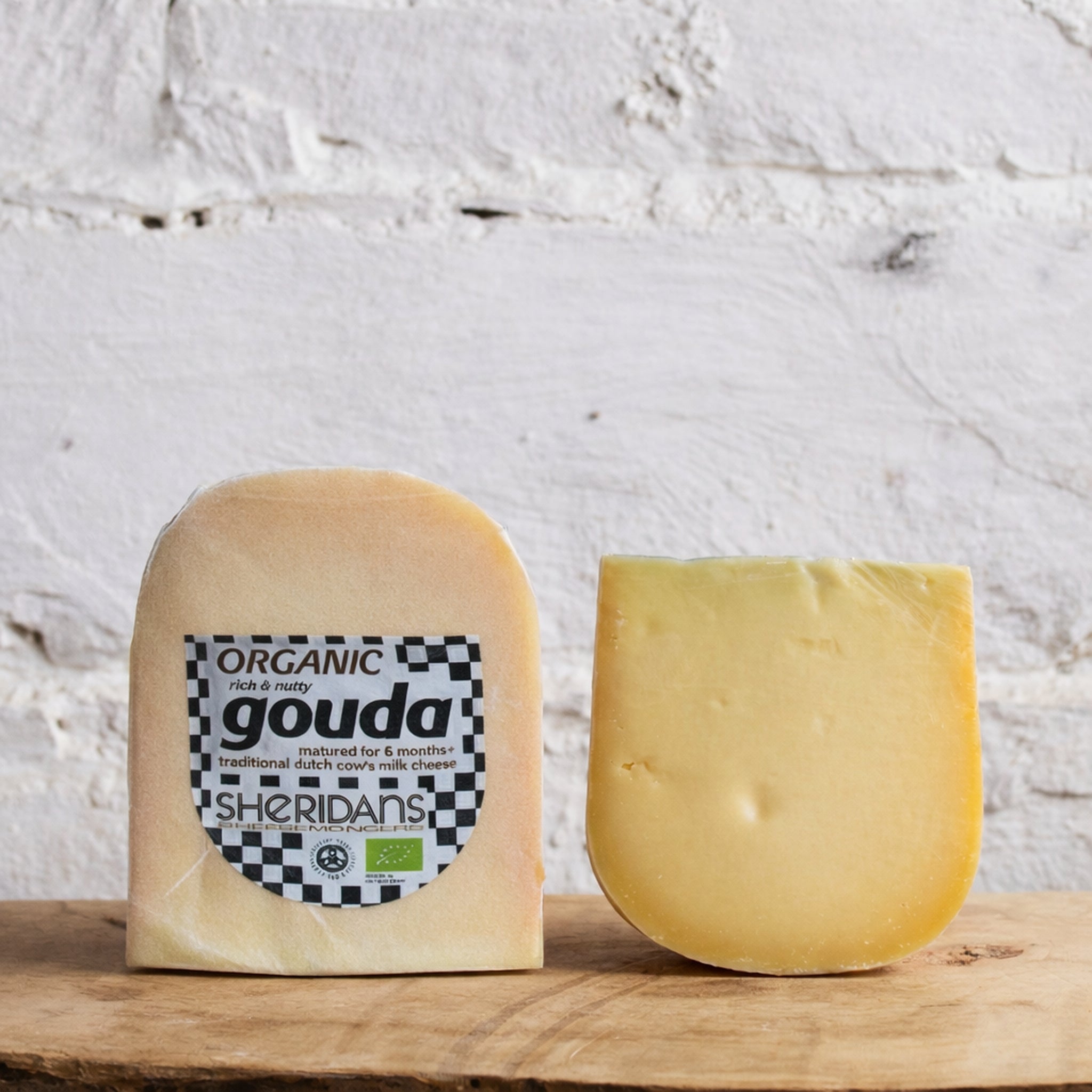 Two blocks of gouda cheese with a Sheridan's label on a wooden surface against a textured white wall.