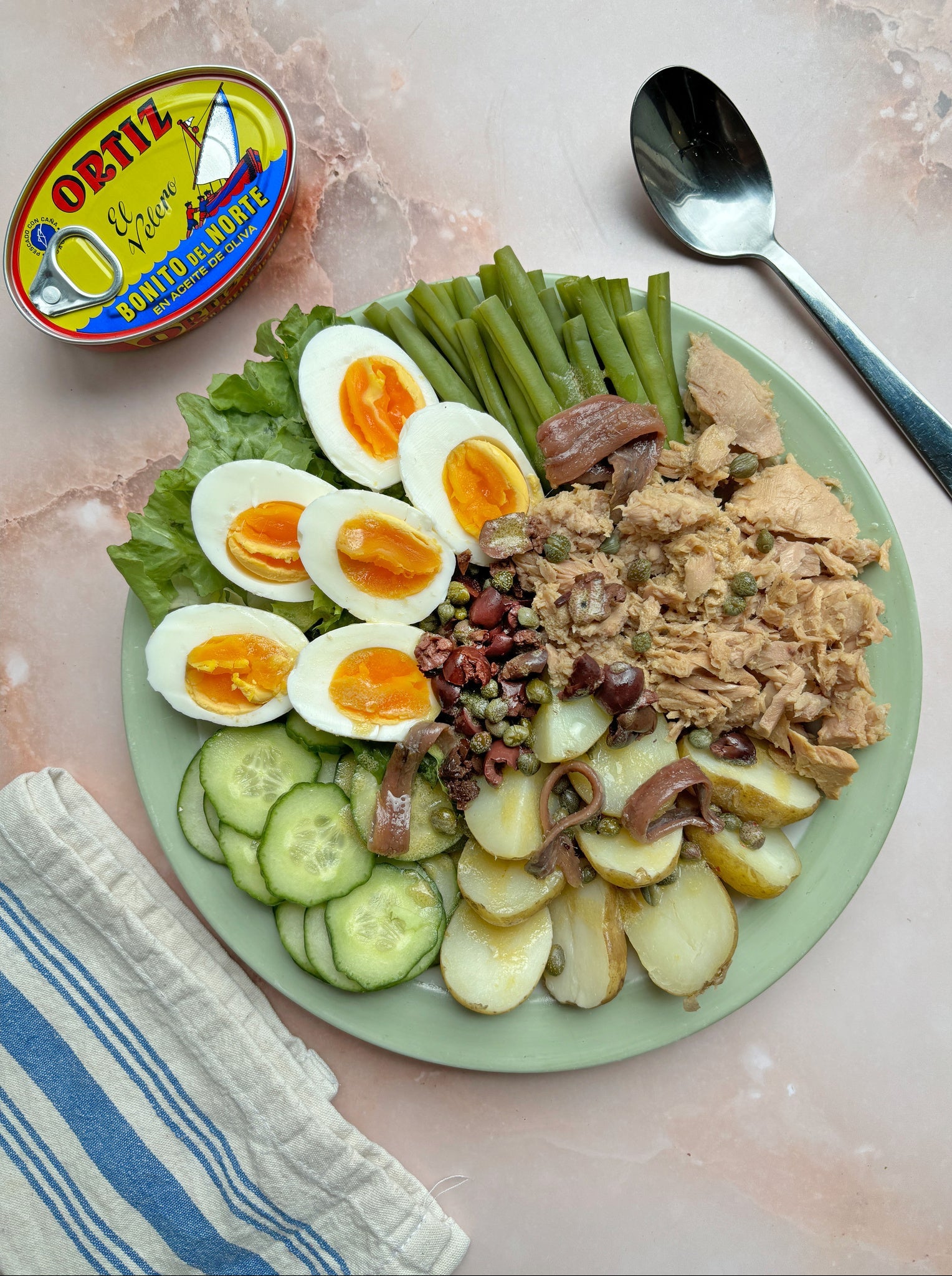 Plated salad with hard-boiled eggs, green beans, and tuna next to a can of Oster tuna.