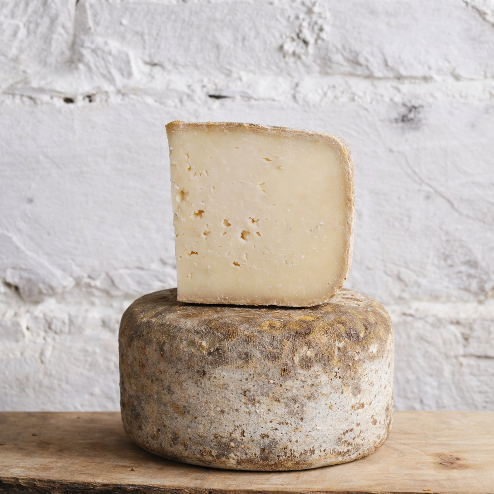 Cheese wheel with a piece of cheese on top against a textured white background