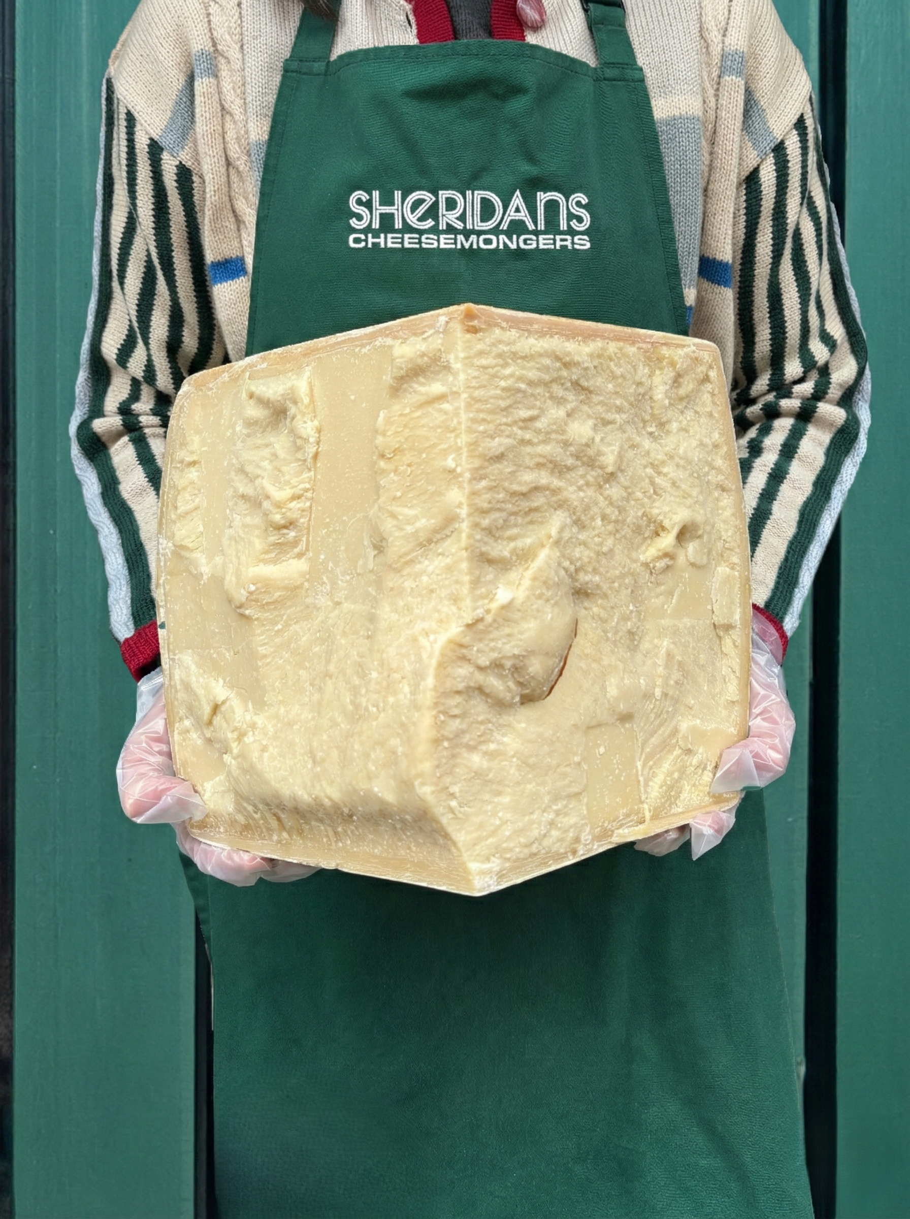 Person wearing a Sheridan's Cheesemongers apron holding a large block of cheese.