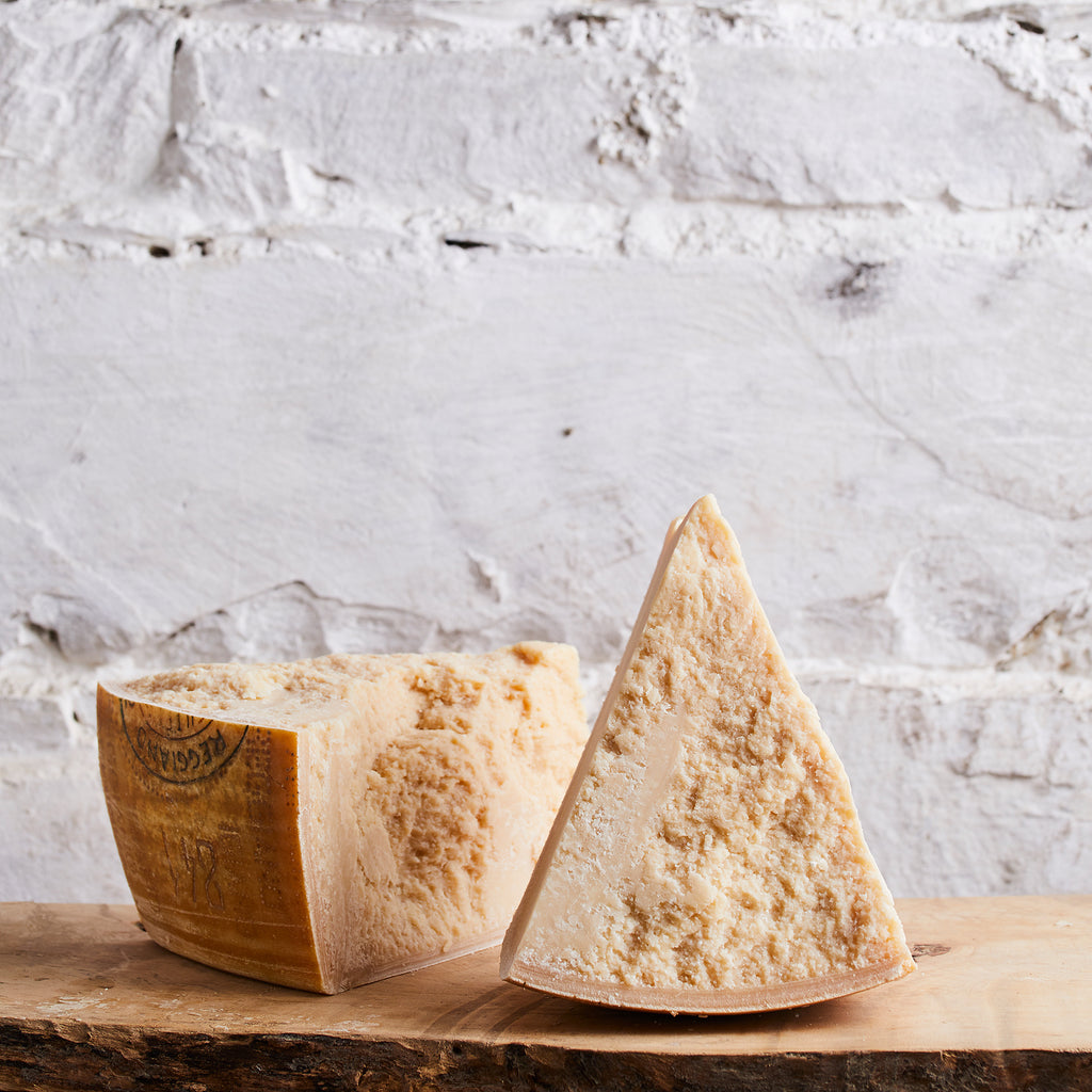 Two blocks of cheese, one whole and one sliced, on a wooden board with a marble background.