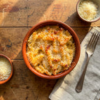 Bowl of macaroni and cheese on a wooden table with a fork and Parmesan cheese.