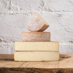 Stack of various types of cheese on a wooden surface with a textured white background