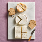 Assorted cheeses and crackers on a marble board with a purple background