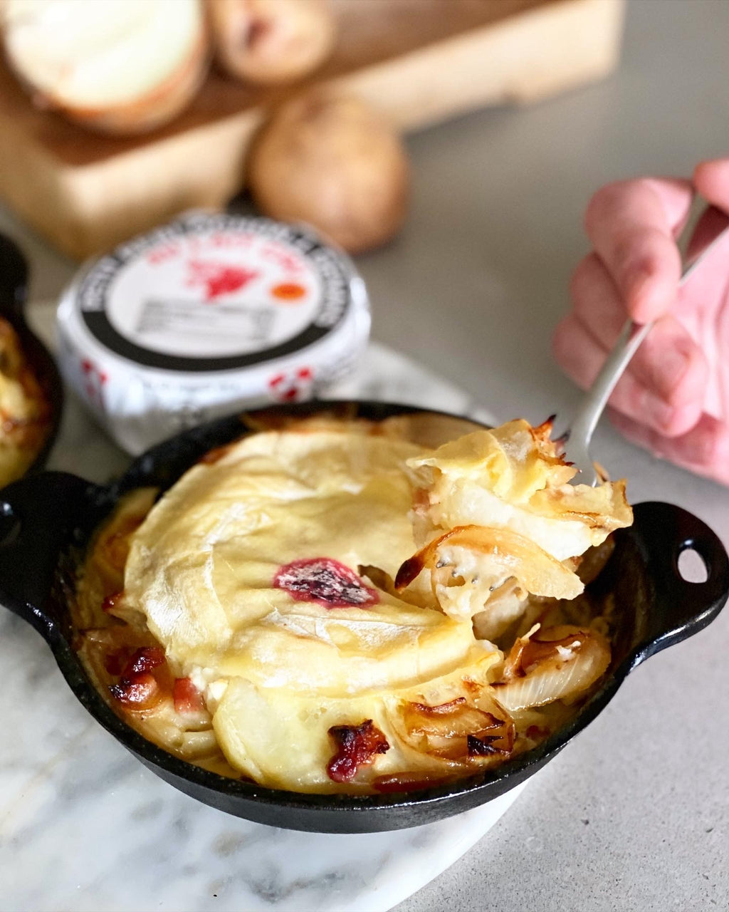 Baked dish with cheese and onions being served with a spoon, surrounded by bread and butter.