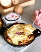 Baked dish with cheese and onions being served with a spoon, surrounded by bread and butter.