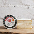 Cheese with a round label on a wooden surface against a textured white wall