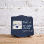 Packaged ricotta cheese with Garofalo label on a wooden surface and white textured wall background