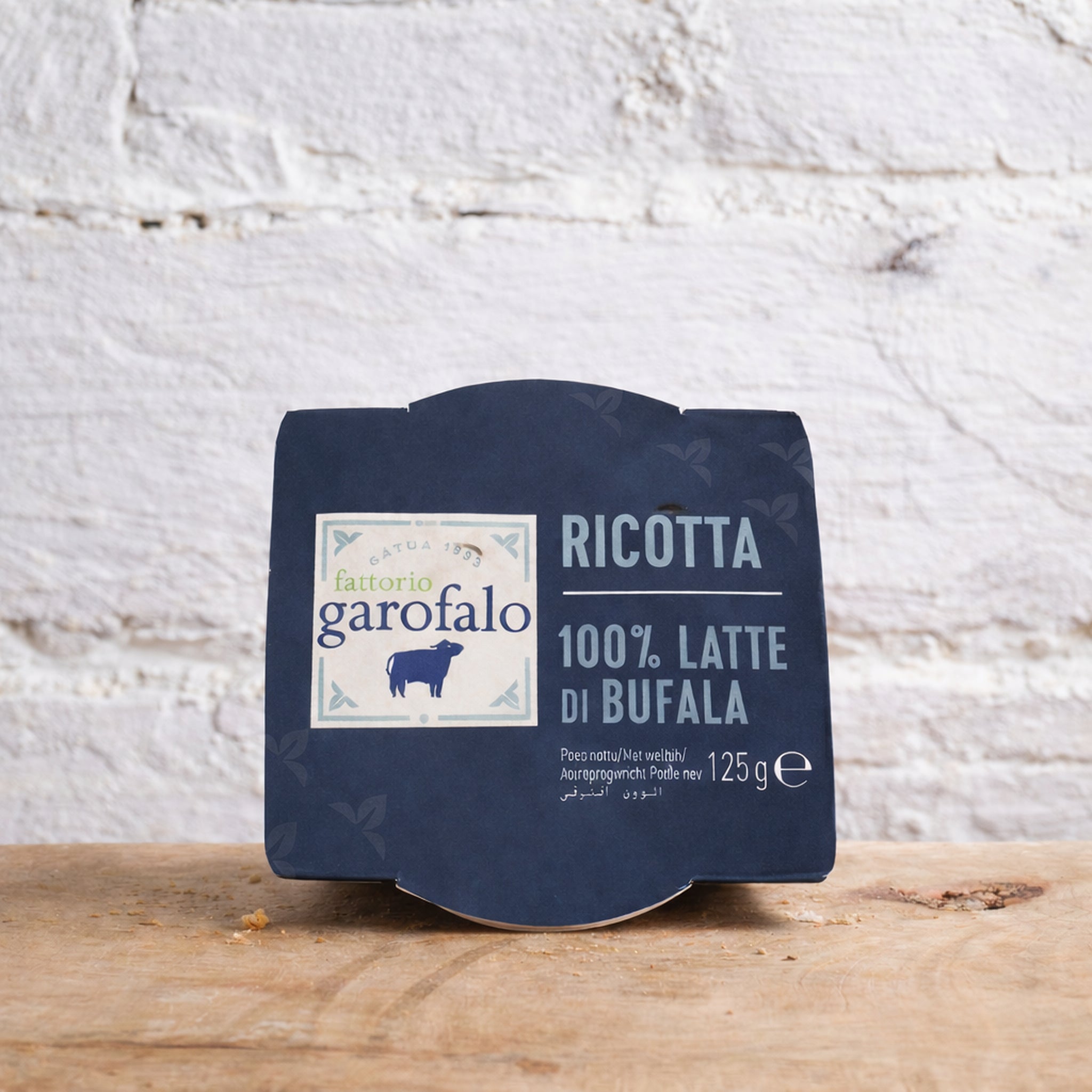 Packaged ricotta cheese with Garofalo label on a wooden surface and white textured wall background