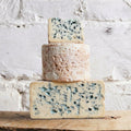 Three types of blue cheese stacked on a wooden surface with a white textured background