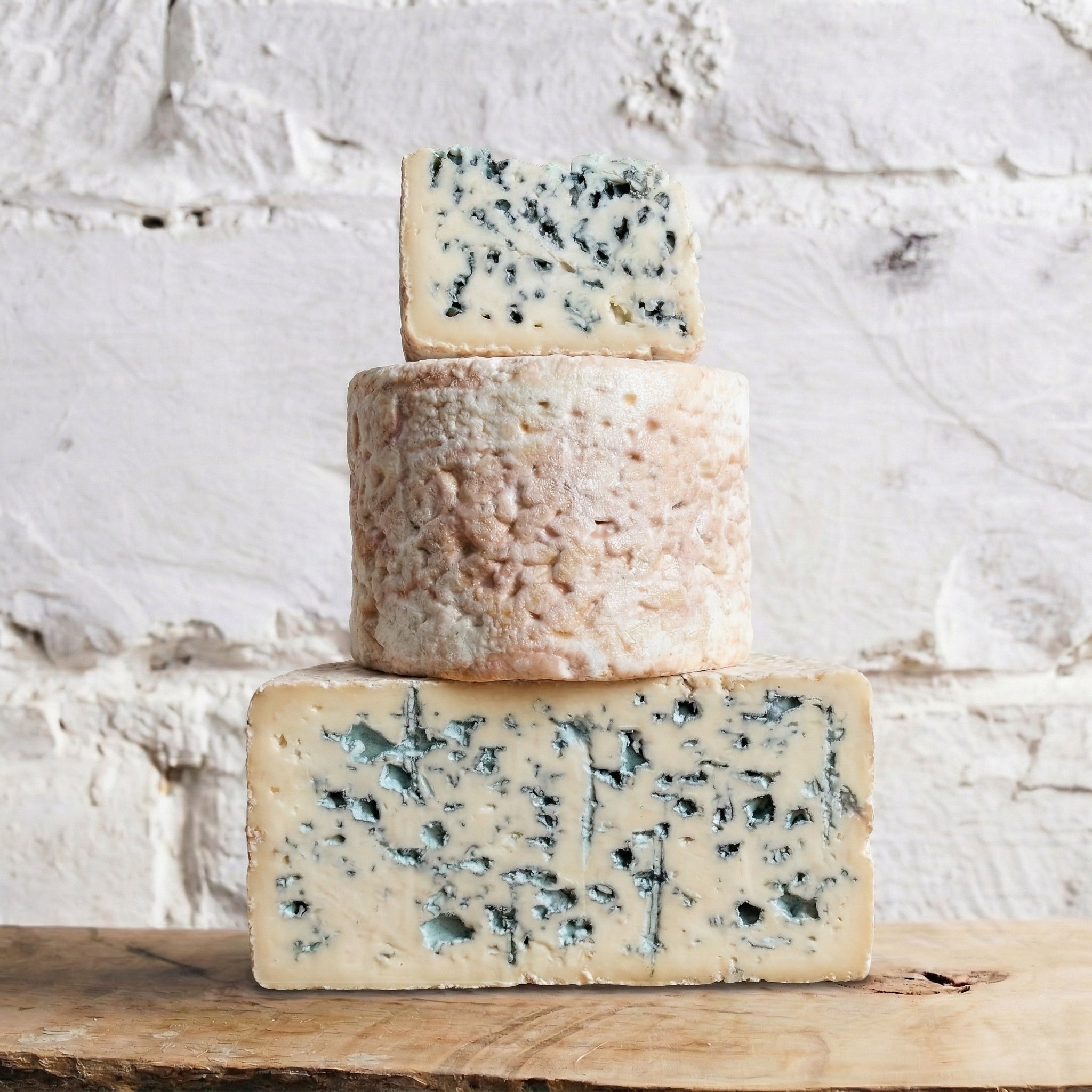 Three types of blue cheese stacked on a wooden surface with a white textured background