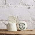 Three blocks of cheese with a label on a wooden surface against a white brick wall.