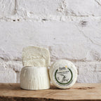 Three blocks of cheese with a label on a wooden surface against a white brick wall.