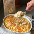 Macaroni and cheese being served with a spoon, next to a package of pasta.