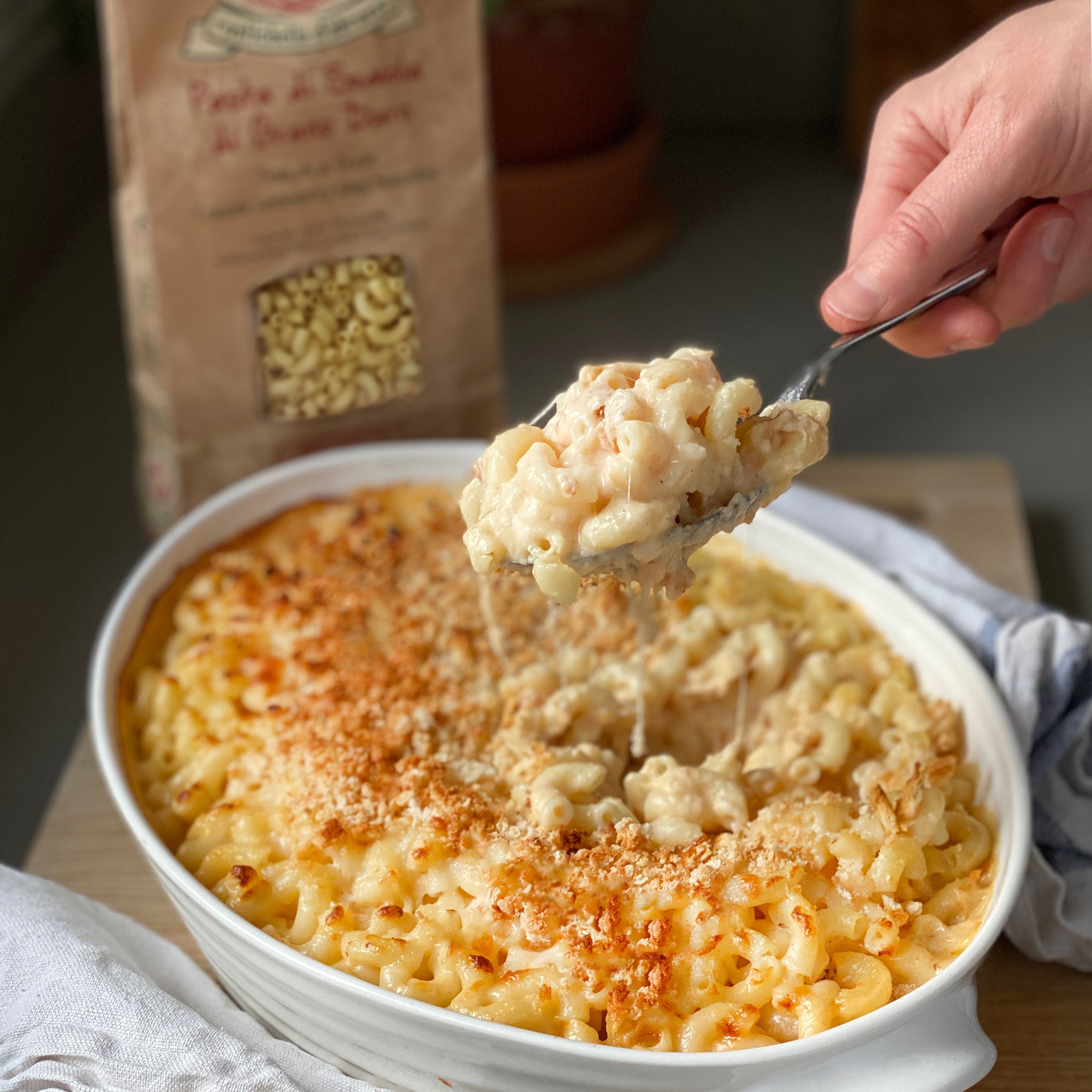 Macaroni and cheese being served with a spoon, next to a package of pasta.
