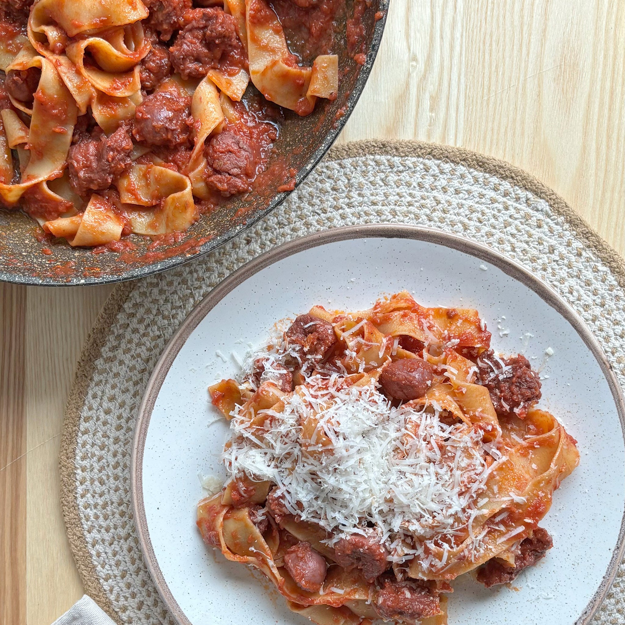 Pasta dish with sauce and parmesan cheese on a plate, next to a pan of pasta.