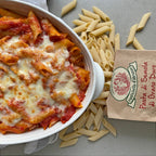 Baked pasta dish with a package of Semola pasta on a gray surface
