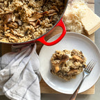 Mushroom risotto in a red pot with a serving on a white plate, accompanied by Parmesan cheese.