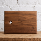Walnut serving board with a hanging hole against a white brick wall