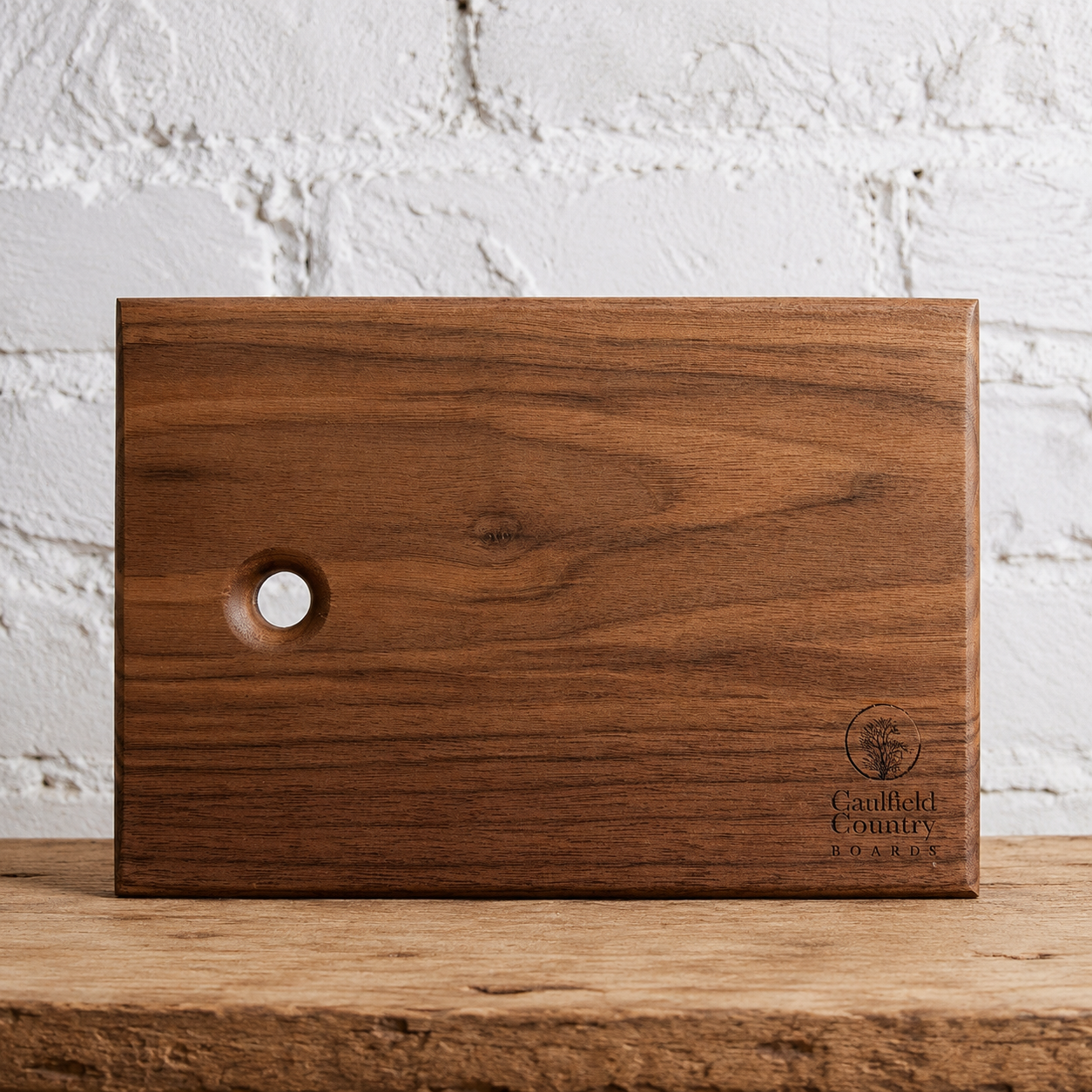 Walnut serving board with a hanging hole against a white brick wall