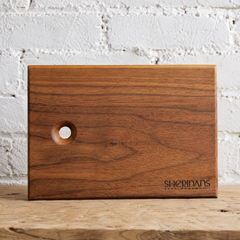 Sheridans walnut wooden serving board against a white brick wall