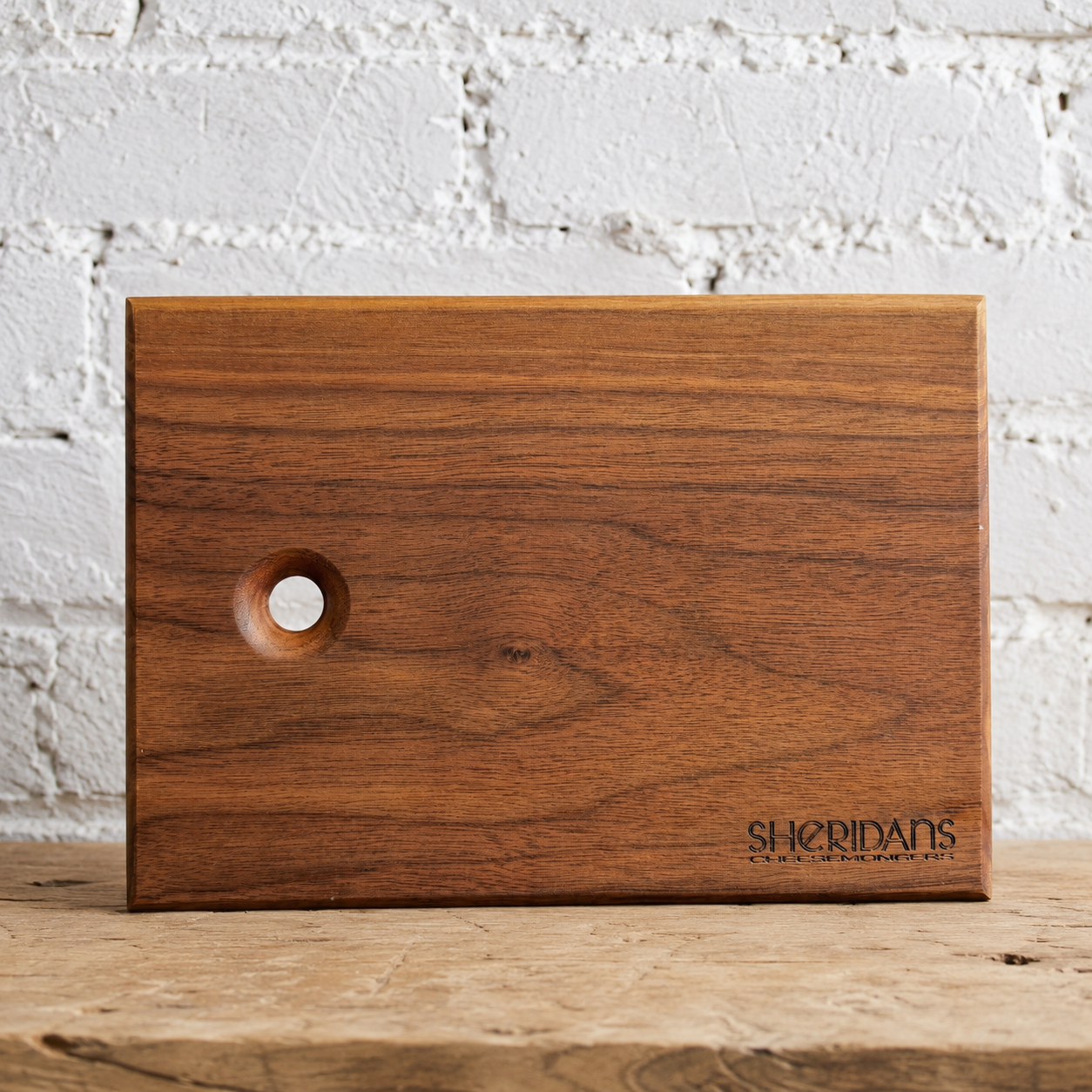 Sheridans walnut wooden serving board against a white brick wall