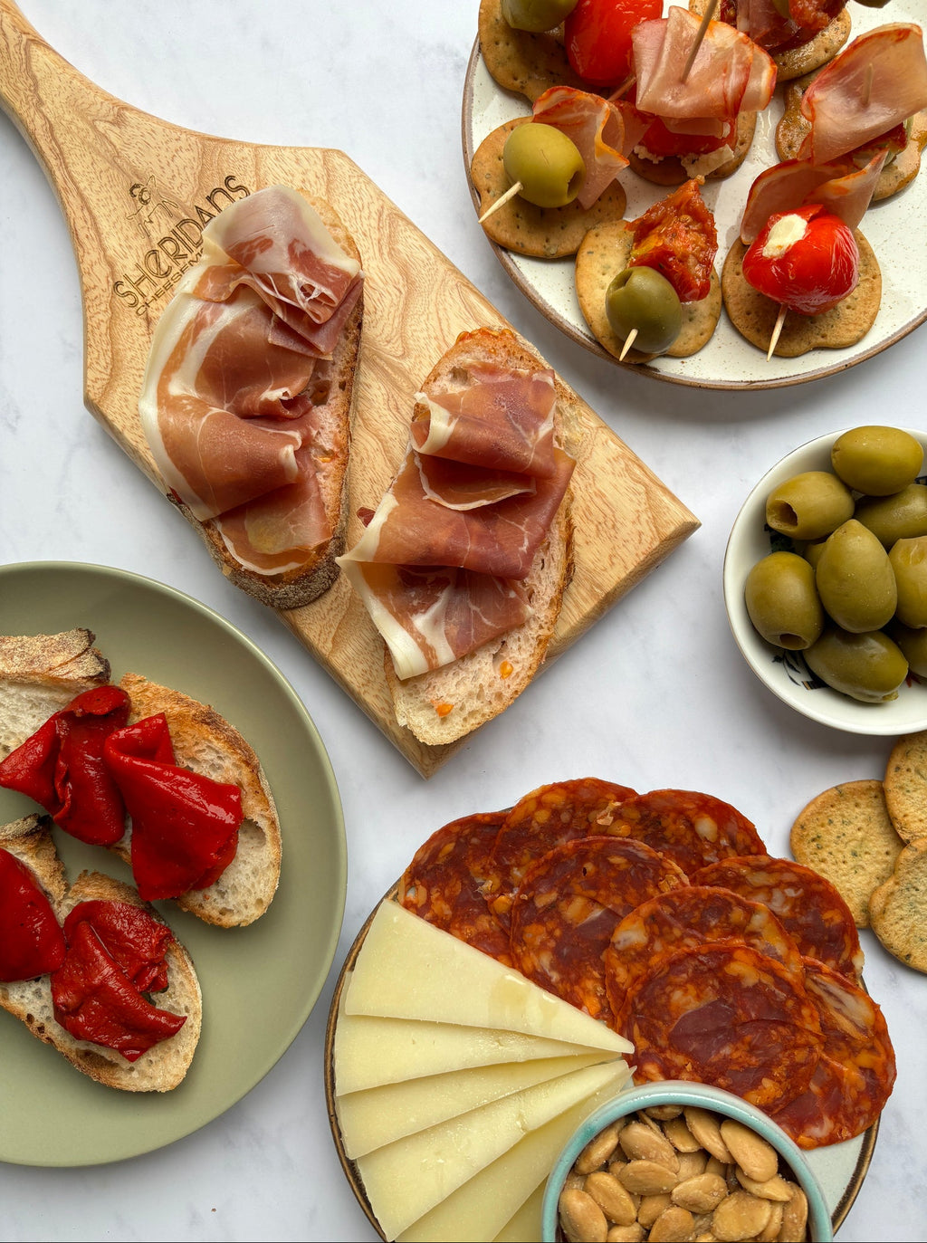 Assorted tapas including cured meats, olives, and cheese on a marble surface.
