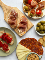 Assorted tapas including cured meats, olives, and cheese on a marble surface.