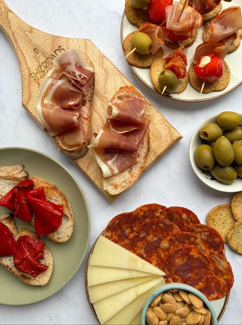 Assorted tapas including cured meats, olives, and cheese on a marble surface.