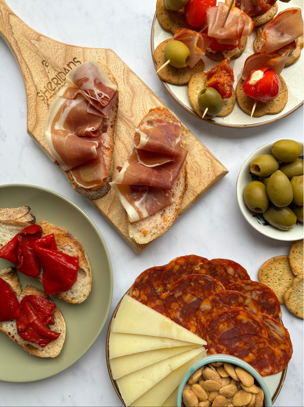 Assorted tapas including cured meats, olives, and cheese on a marble surface.