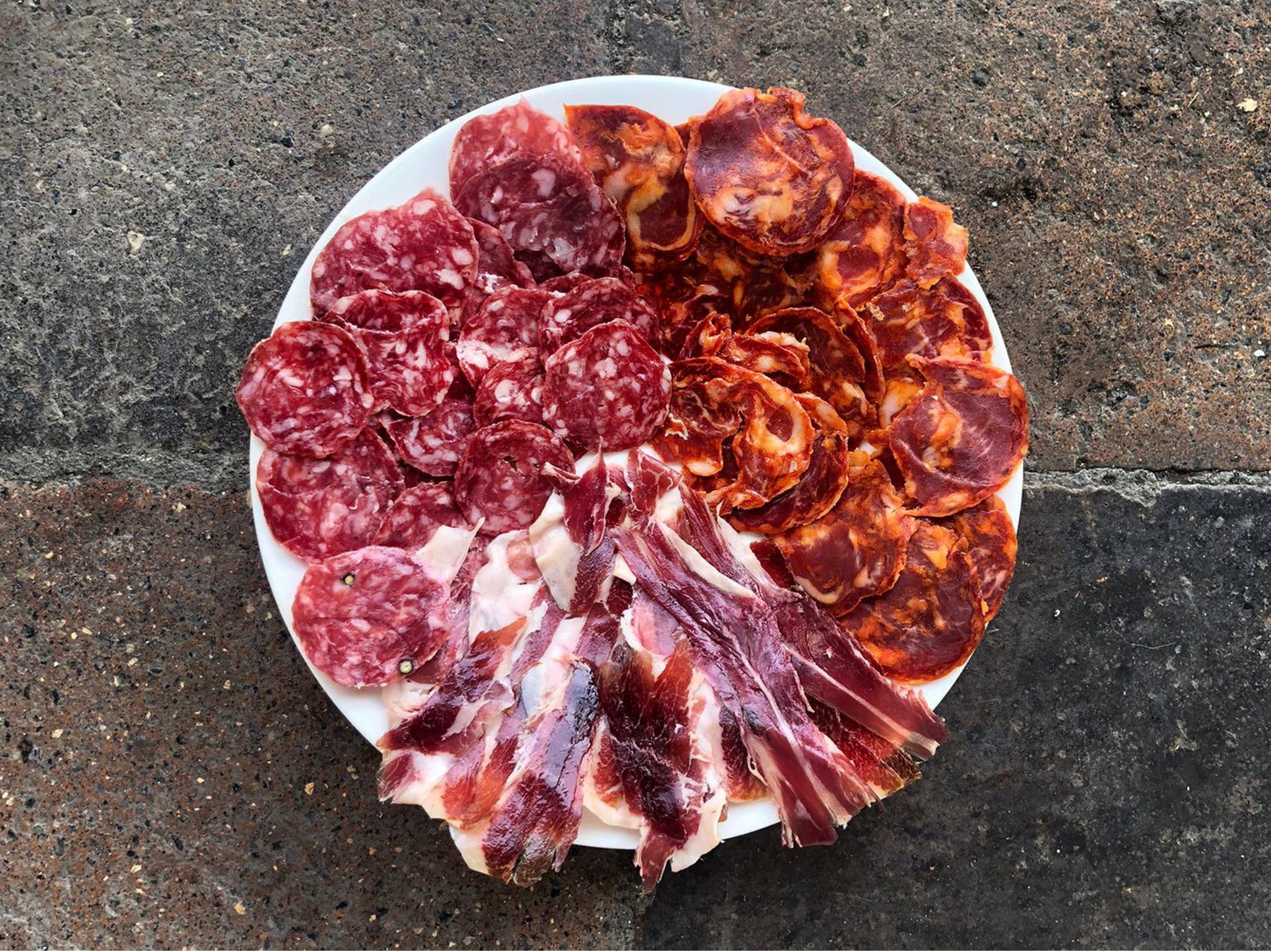 Assorted cured meats on a white plate against a concrete background