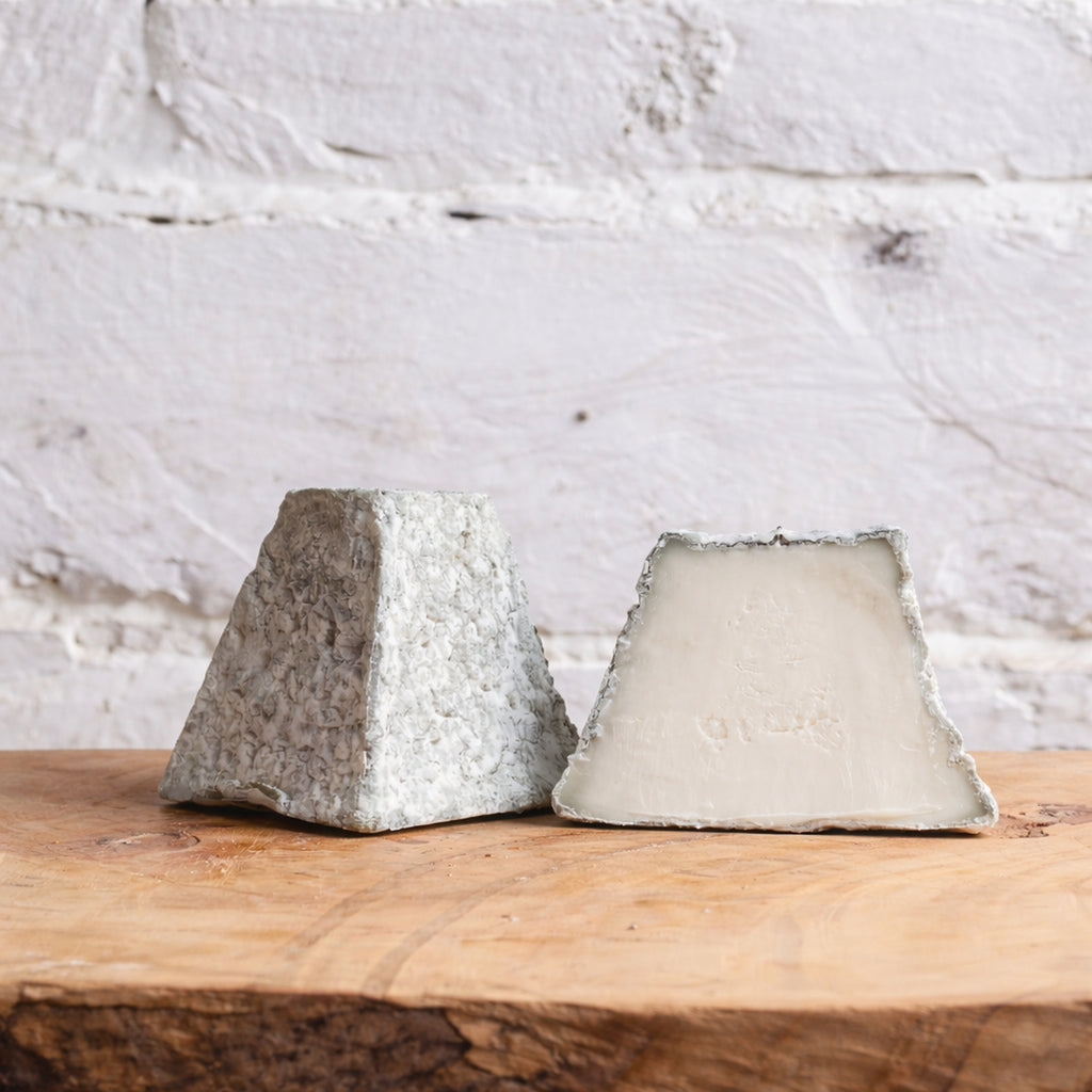 Two blocks of cheese on a wooden surface with a white marble background