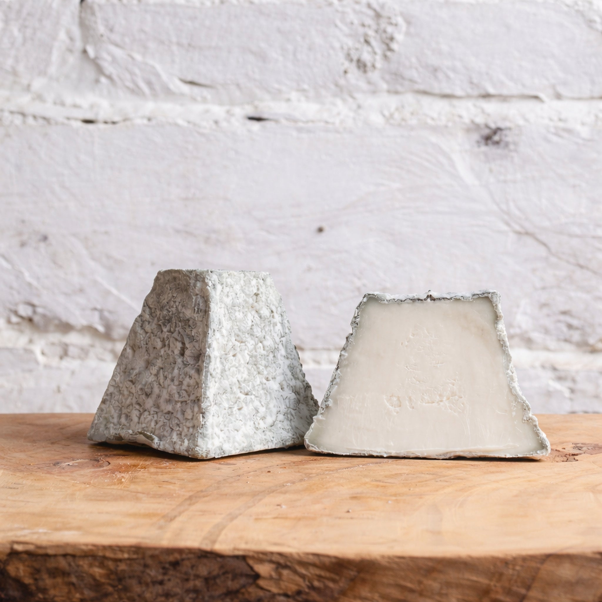 Two blocks of cheese on a wooden surface with a white marble background
