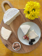Cheese platter with a wedge of cheese, figs, blackberries, and a small bowl of nuts on a wooden board.