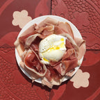 Hard-boiled egg with prosciutto on a white plate on a red textured surface