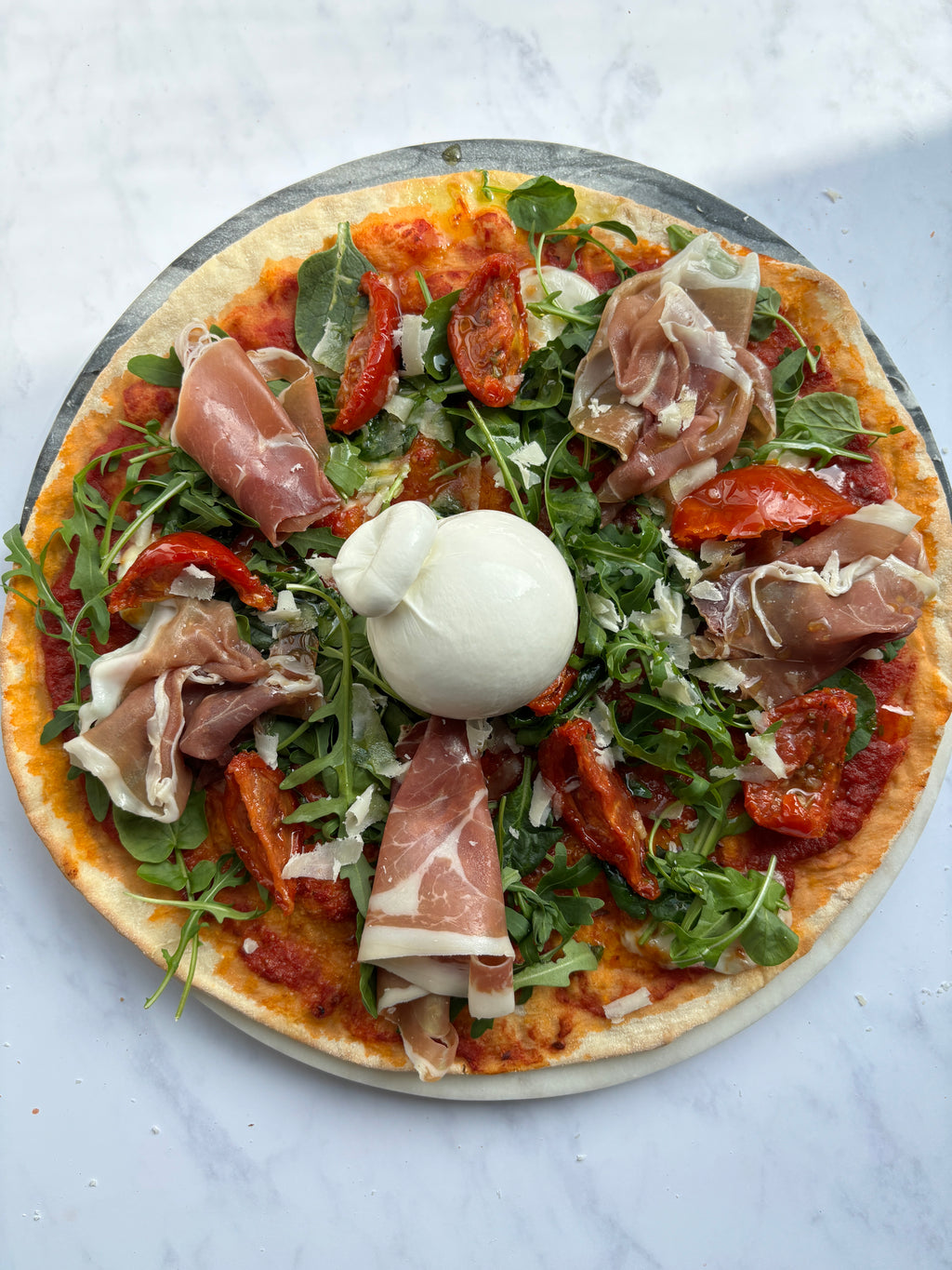 Uncooked pizza with prosciutto, arugula, and a poached egg on a marble surface